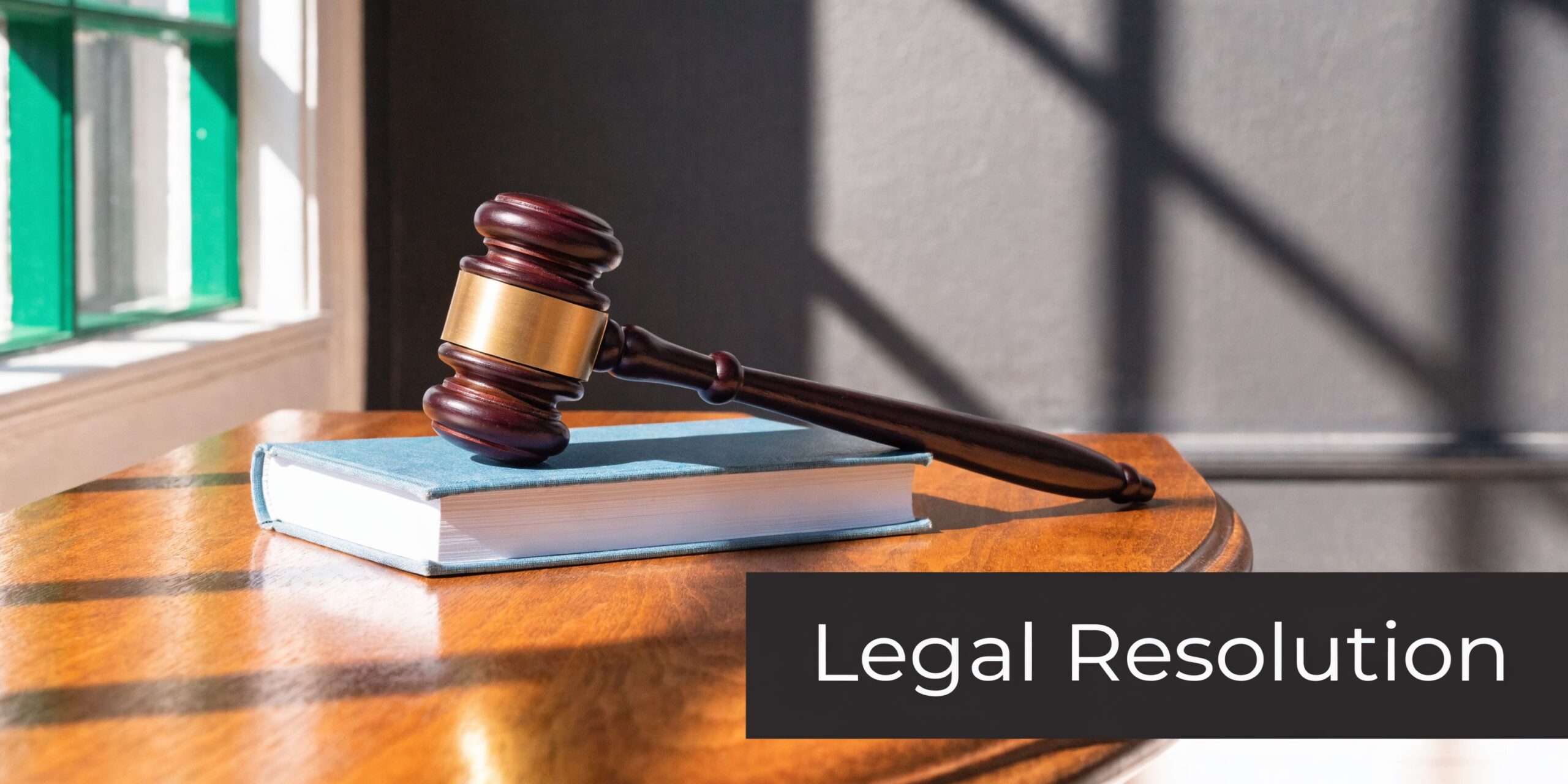 A wooden gavel rests on a blue law book on a wooden table, symbolizing legal resolution.