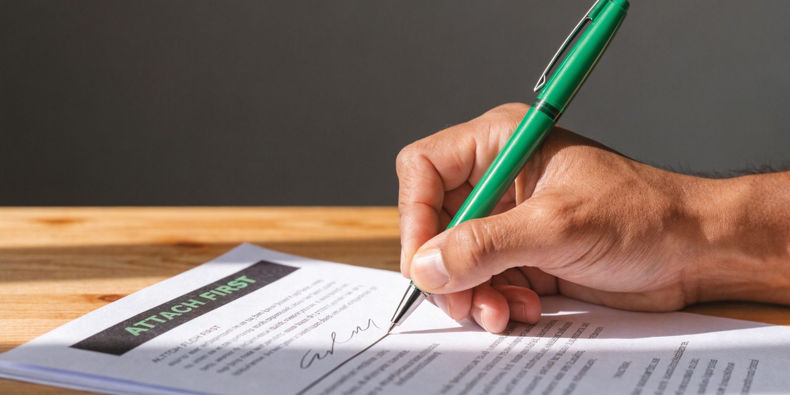 A close-up shot of a person's hand using a green pen to sign a legal document.