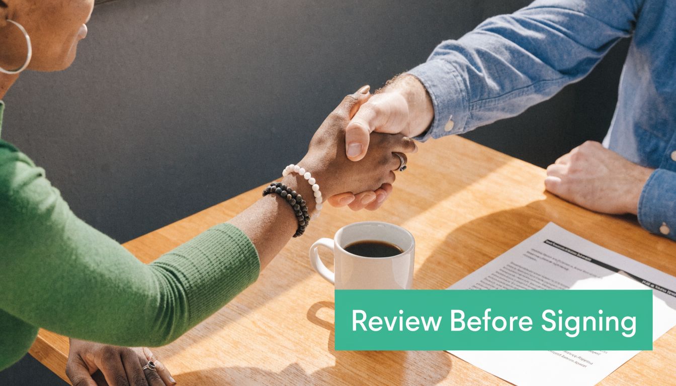 A close-up of two professionals shaking hands over a business contract at a wooden table.
