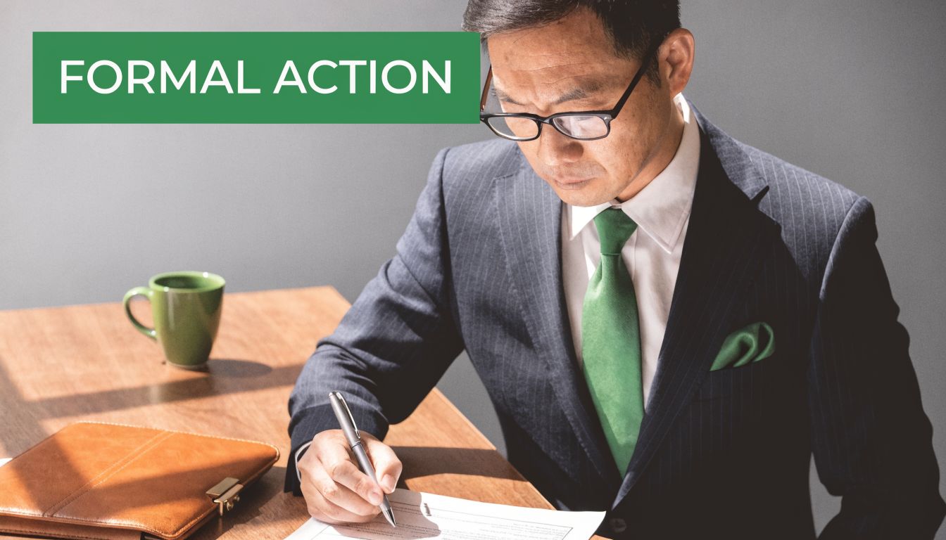 A professional businessman in a suit and green tie signing a formal corporate resolution document at his desk.
