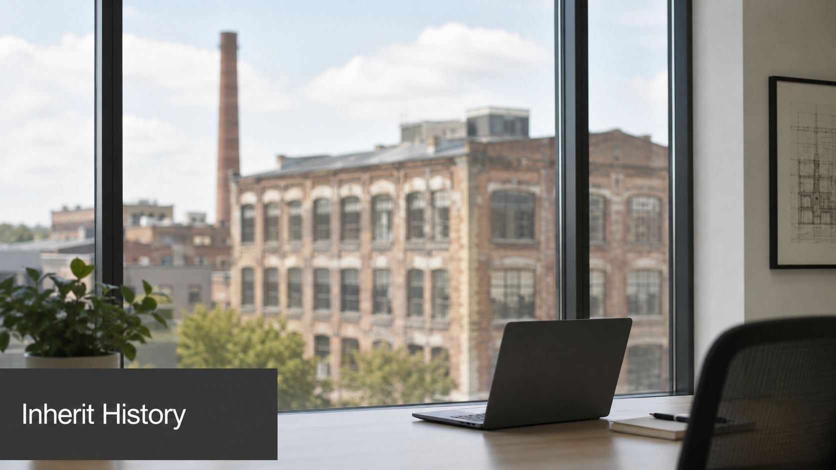 A modern office desk with a laptop and plant overlooking an old historic industrial brick building.